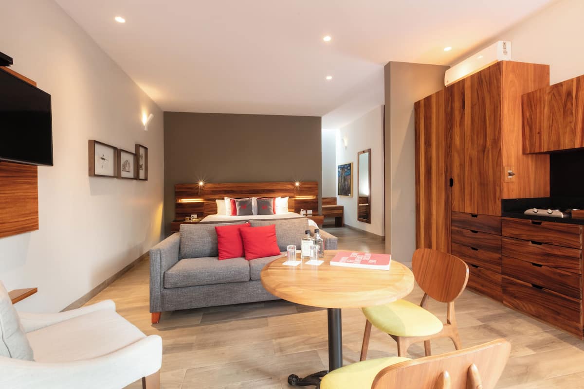 A modern living room with a sofa, chairs, a round table, and a kitchen area with wooden cabinets.