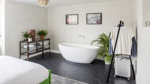 Une salle de bain moderne avec une baignoire sur pieds, un meuble en verre orné de plantes et une valise.