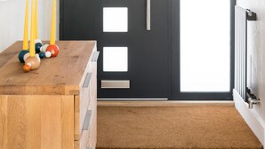 Un intérieur moderne avec une porte sombre, une table d’appoint en bois agrémentée d’objets décoratifs et un radiateur fixé au mur.