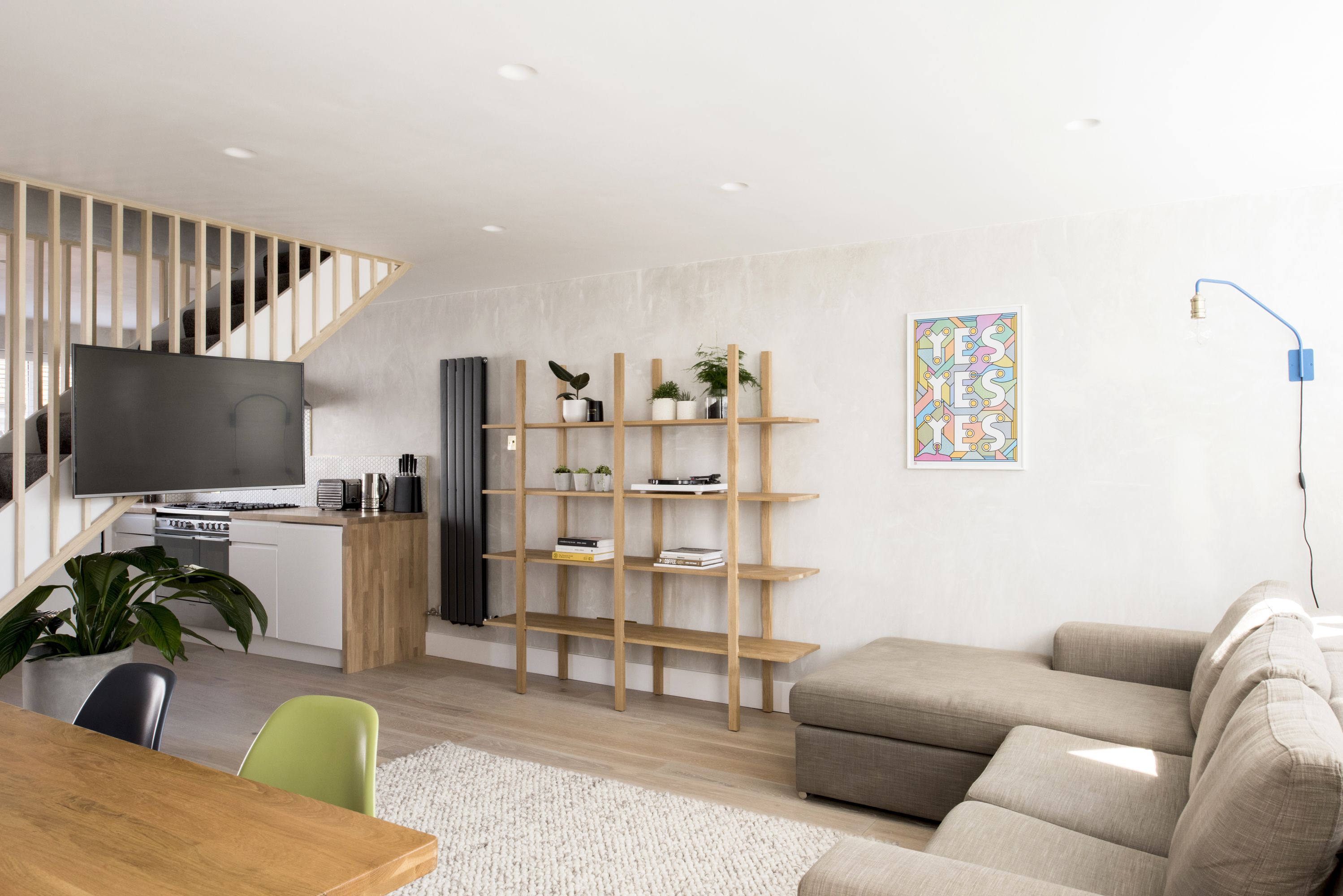Een moderne woonkamer met een houten trap, een flatscreen televisie, een houten boekenkast en een bank.