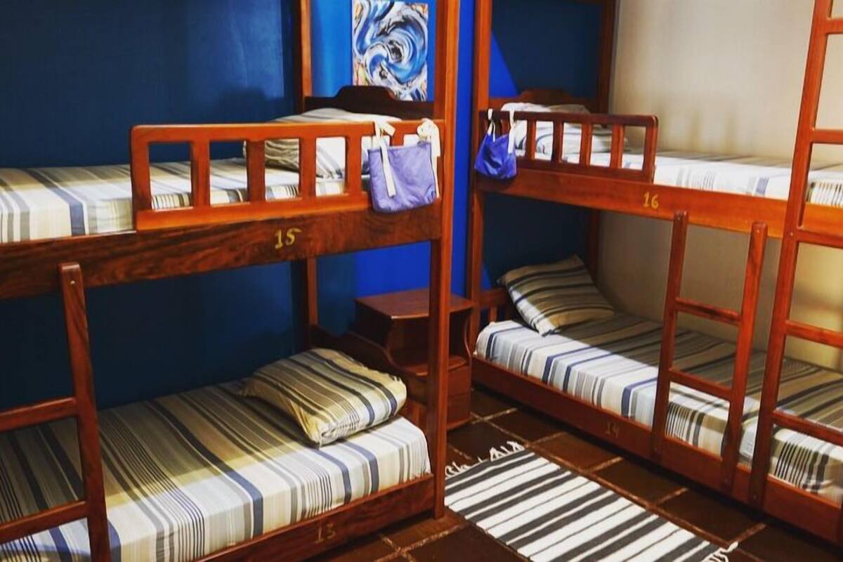 Beliches com roupa de cama listrada, grades de madeira e parede azul.