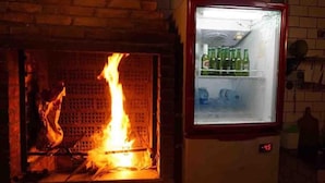Una chimenea de ladrillo con fuego encendido y un refrigerador con botellas de cerveza encima.