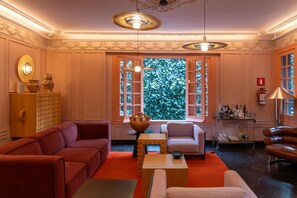 Ein gut beleuchteter Raum mit einem roten Sofa, einem weißen Sessel und einem Couchtisch aus Holz. Ein großes Fenster bietet Blick auf viel Grün.