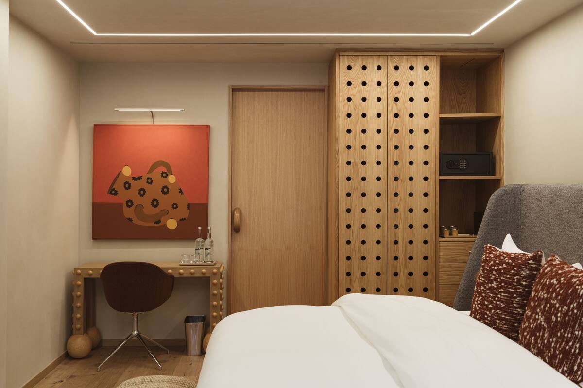 Une chambre d’hôtel comprenant un lit, un bureau avec une chaise, une armoire et une œuvre d’art accrochée au mur.