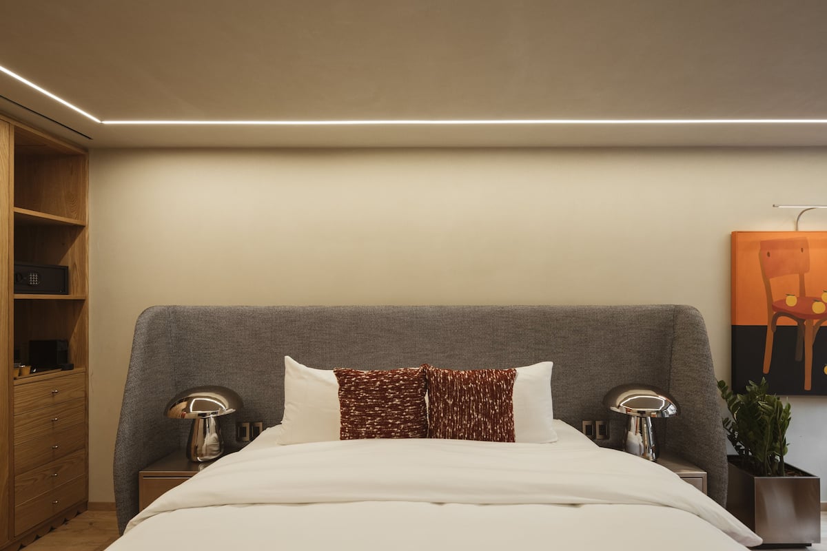 Une chambre d’hôtel moderne avec un grand lit, deux tables de chevet avec des lampes, une commode en bois et une œuvre d’art accrochée au mur.