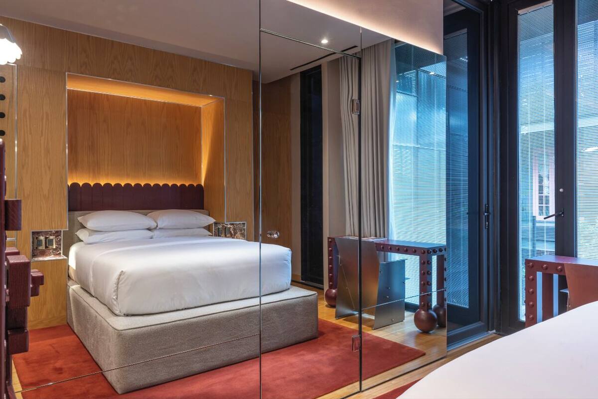 Une chambre d’hôtel moderne dotée d’un grand lit, d’une paroi en verre et d’une vue sur la ville.