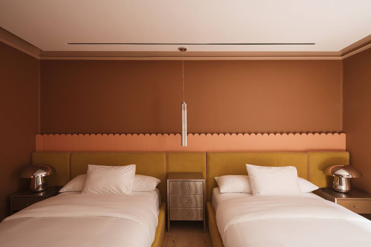Une chambre d’hôtel avec deux lits, une table de chevet, une lampe et une commode.