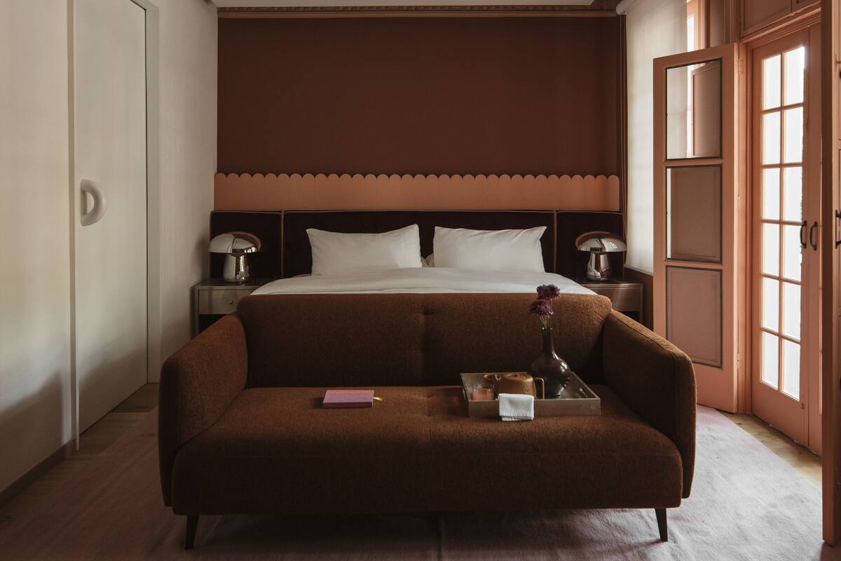 Une chambre à coucher avec un lit, un canapé marron, une table de chevet avec une lampe et une fenêtre donnant sur un beau paysage.