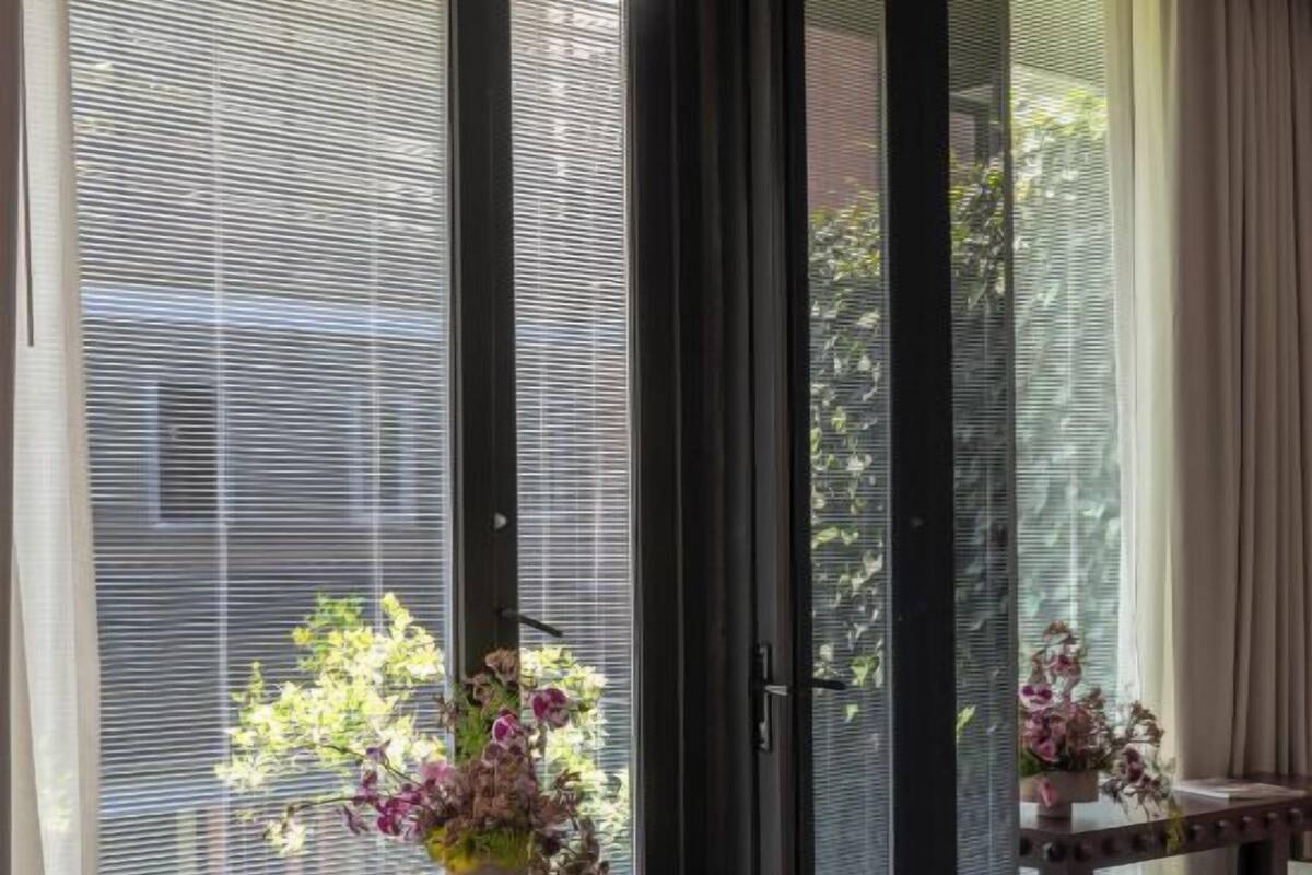 Une chambre moderne dotée d’une grande porte-fenêtre coulissante donnant sur un balcon, d’une table en bois ornée d’un vase de fleurs et d’une chaise.