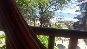 A view from a window overlooking a beach with thatched-roof structures and a tree.