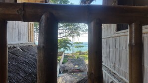 A view through a bamboo-framed window of a thatched-roof structure with a sandy ground and a palm tree in the background. - La Facha Hostel Restaurant Surf (Muisne)