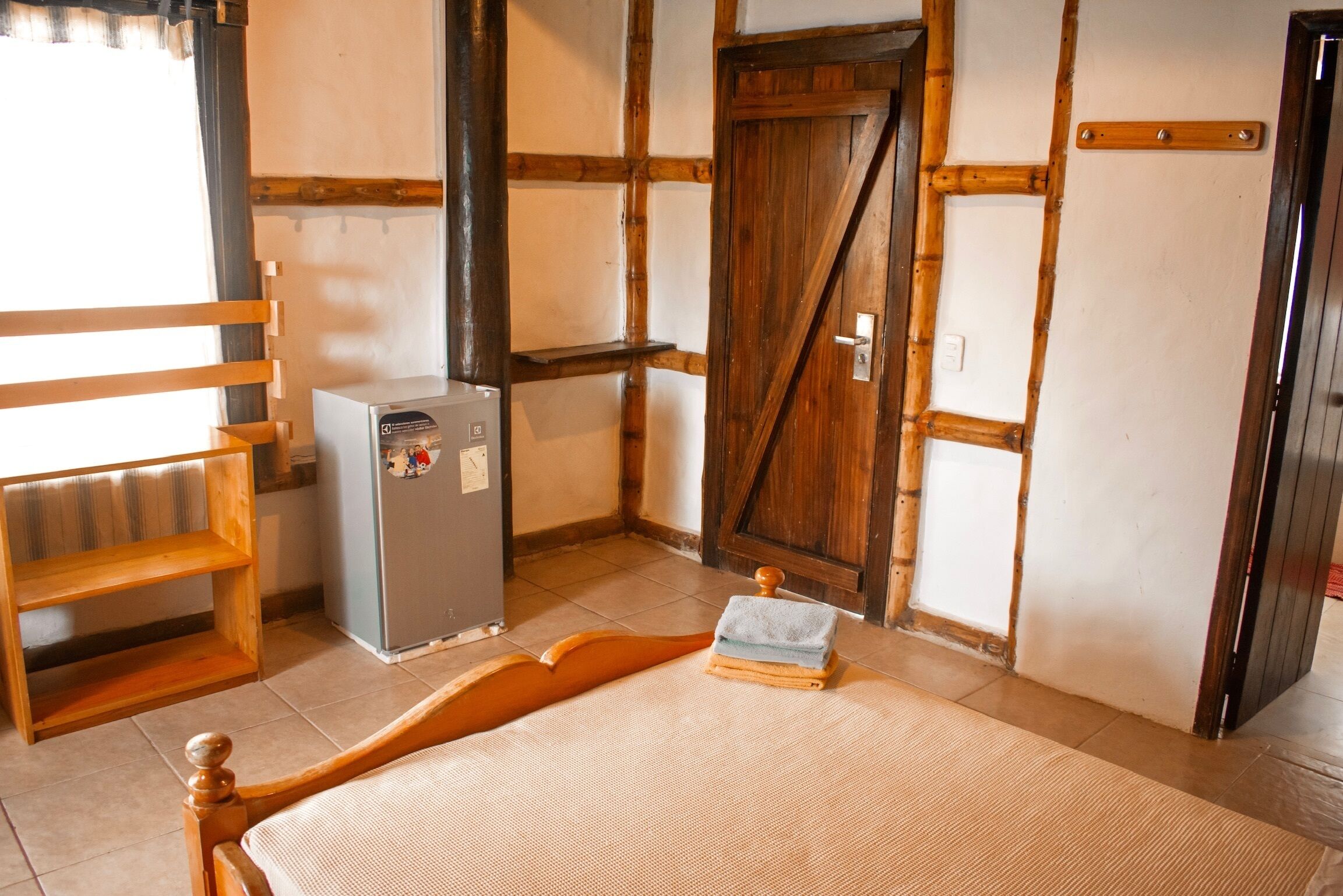 A room with a bed, a wooden shelf, a small refrigerator, and a wooden door.