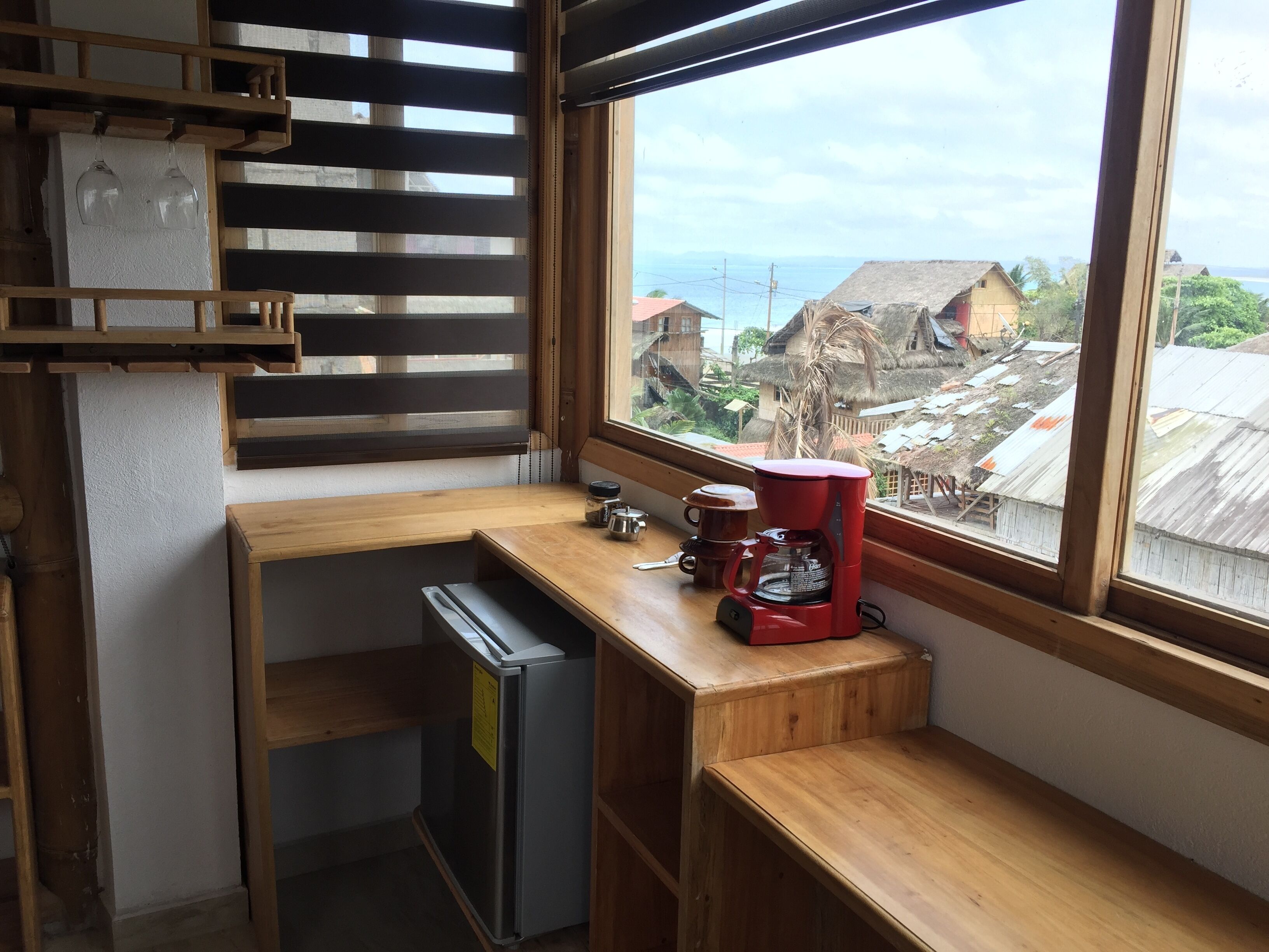 Cocina compacta con refrigerador integrado, cafetera y ventana con vista a una zona residencial.