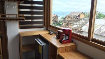 Cocina compacta con refrigerador integrado, cafetera y ventana con vista a una zona residencial.
