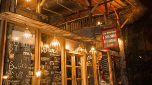 A wooden building with a thatched roof, illuminated by hanging lights. A sign indicates it is a restaurant named "La Finca." - La Facha Hostel Restaurant Surf (Muisne)