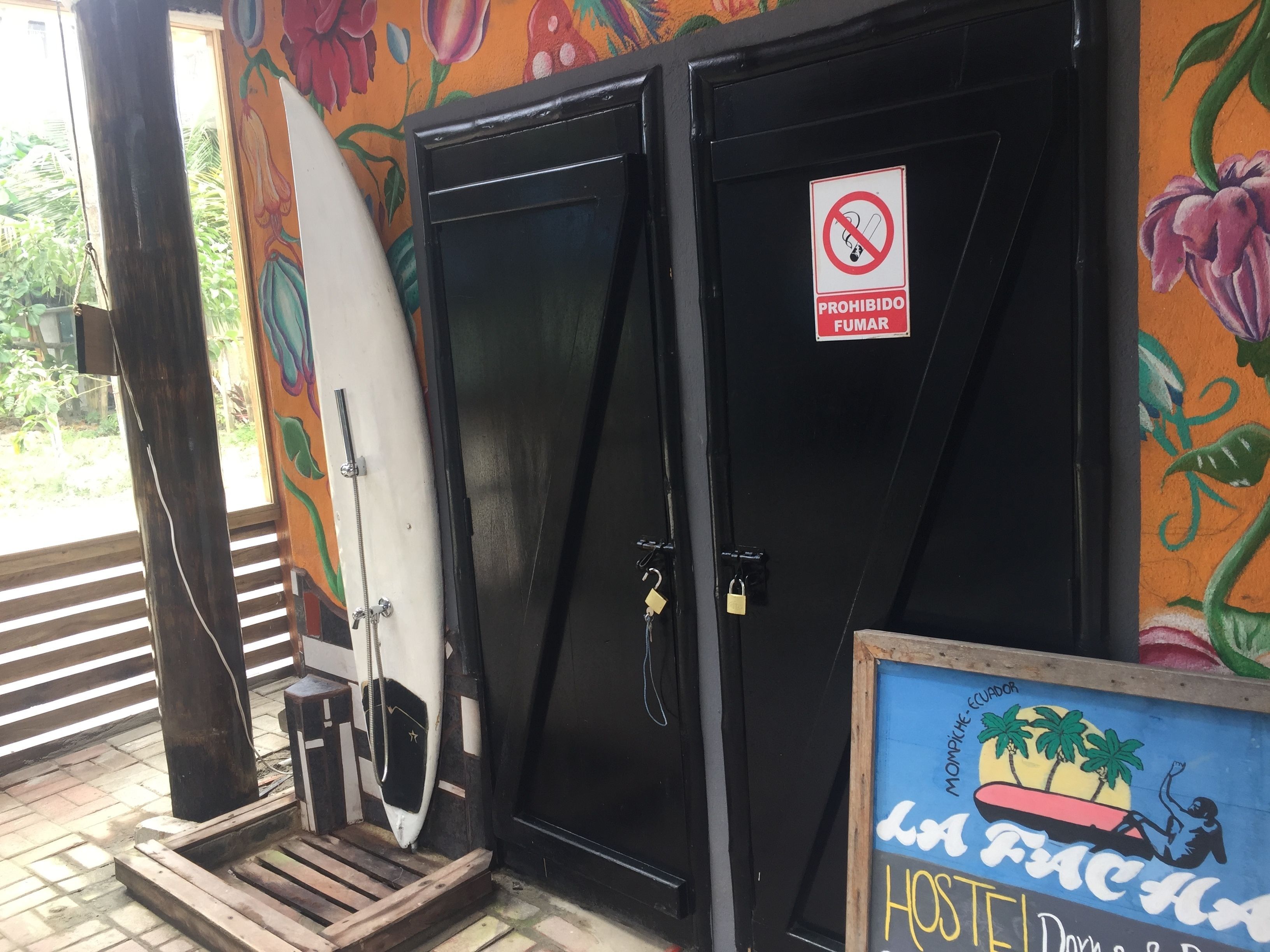 A hotel entrance with a black door, a surfboard leaning against it, and a sign prohibiting smoking.