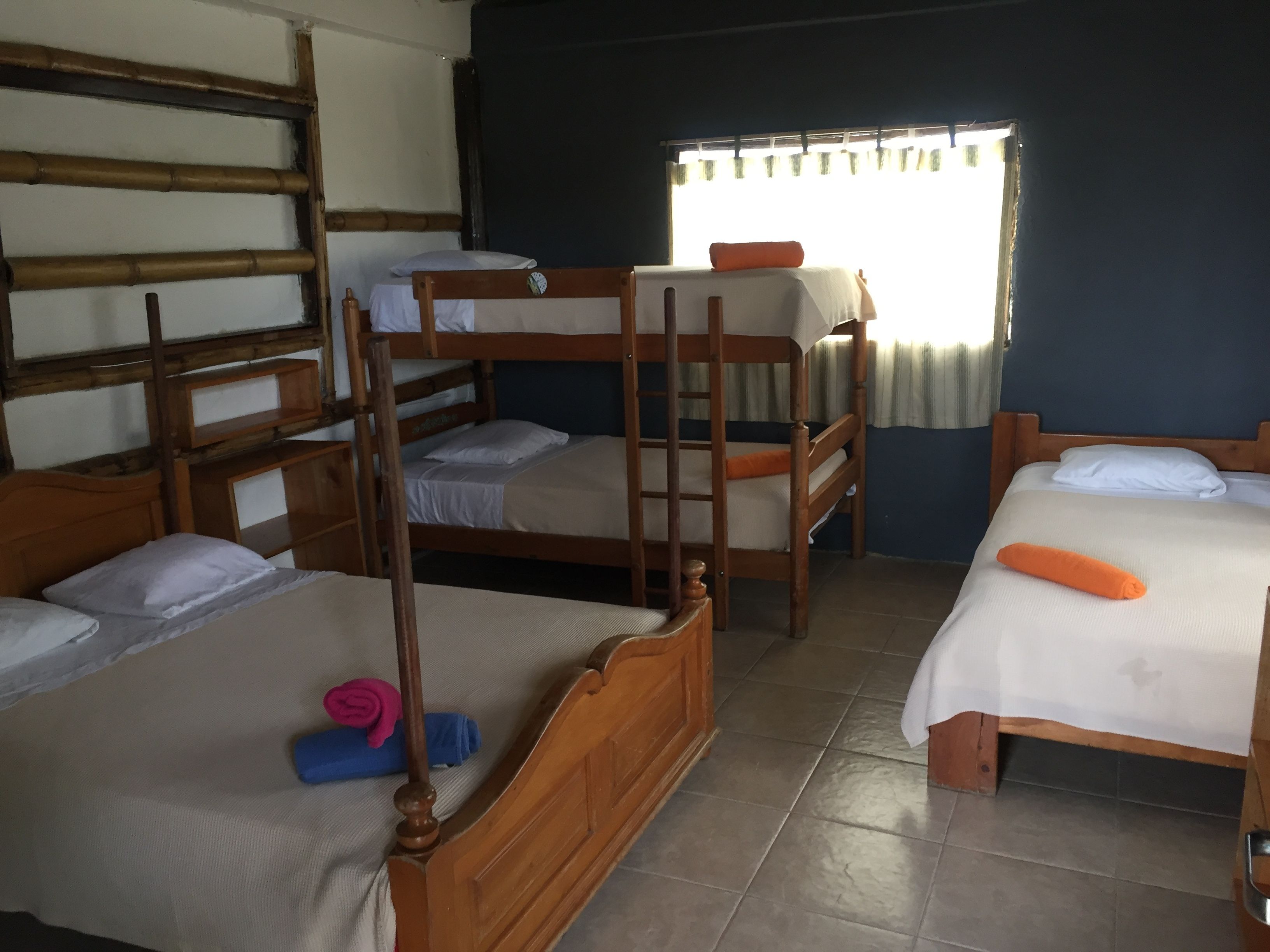 Habitación con literas y una cama individual, cabeceros de madera y una ventana con cortinas.