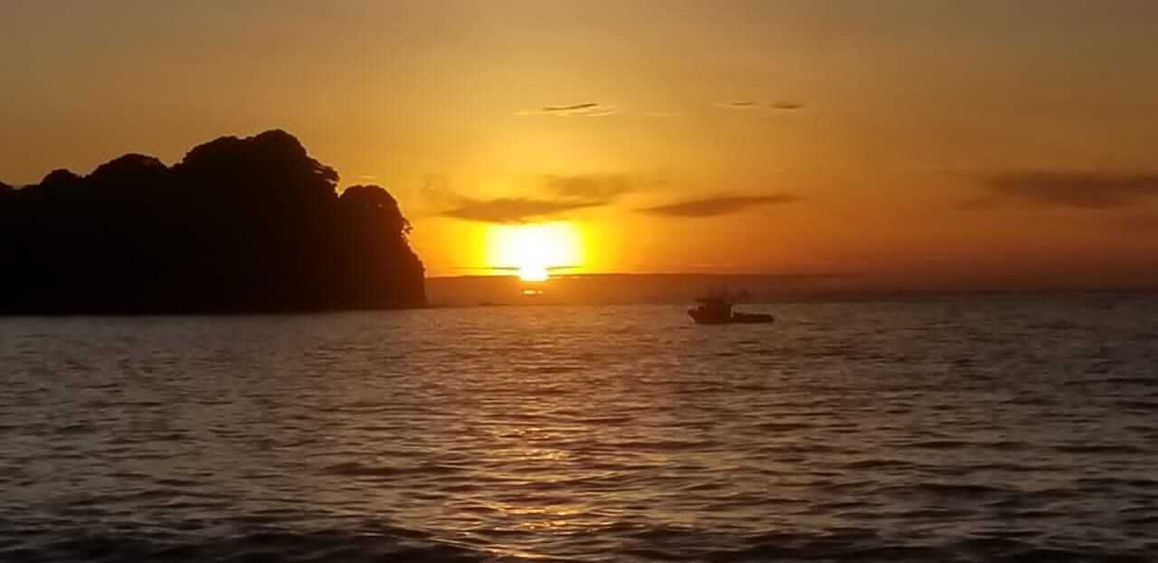 Zonsondergang boven water met een boot en een rotsachtige kustlijn.