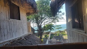 A rustic wooden house with a thatched roof, a large tree in front, and a view of the sea. - La Facha Hostel Restaurant Surf (Muisne)