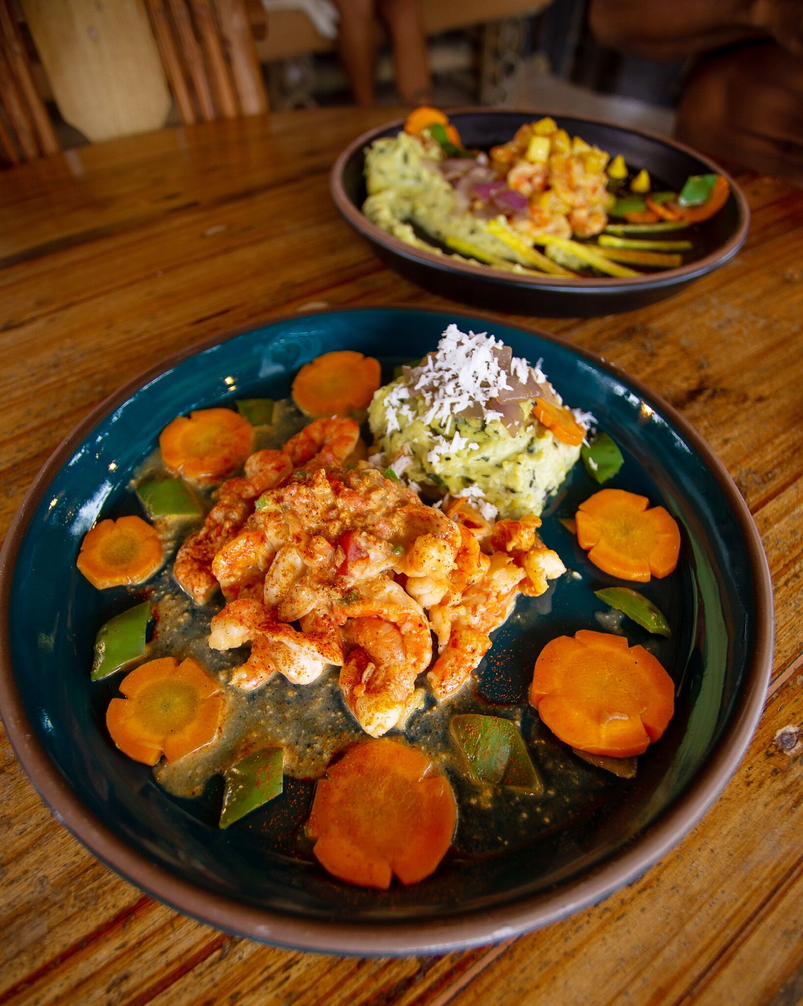 A plate of food with shrimp, vegetables, and a side dish on a wooden table.