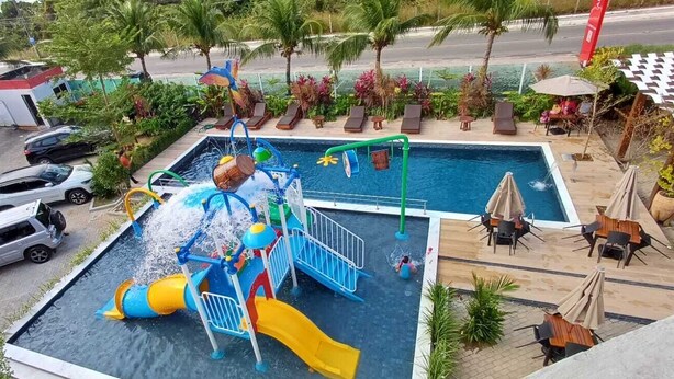 A swimming pool with a water play area, lounge chairs, and a view of palm trees and a road. - Altiplano Hotel (João Pessoa)