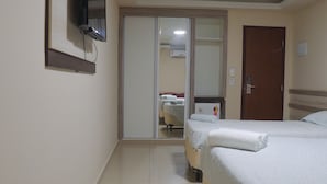 Habitación de hotel con cama, armario, espejo y televisor en la pared.