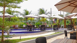 An outdoor seating area with tables and umbrellas, a pool, and tropical plants. - Altiplano Hotel (João Pessoa)