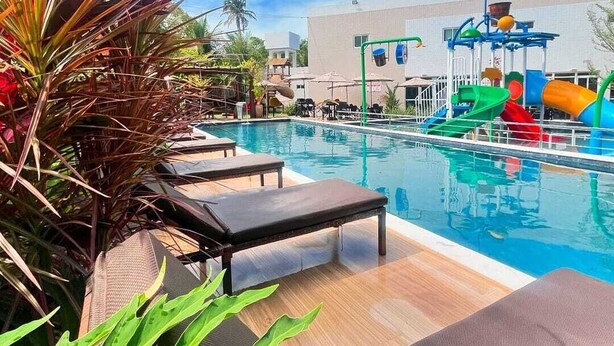 Un área de piscina con sillas de descanso, un tobogán de agua y un puesto de salvavidas.
