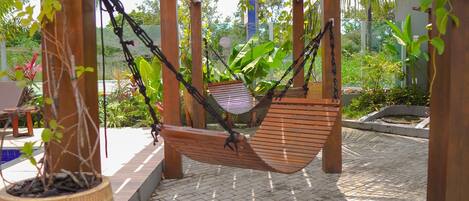 Een hangmat onder een houten pergola in een tuin met potplanten en een betegeld terras.