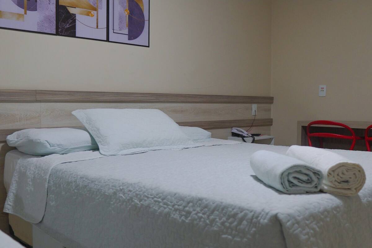 Une chambre d’hôtel avec un lit, des oreillers, un téléphone et deux chaises rouges.
