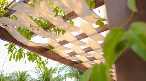 Una estructura de pérgola de madera con diseño de celosía, rodeada de follaje verde.