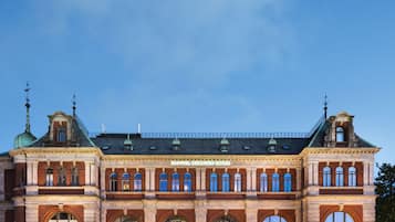 A historic building with arched windows and a central entrance, featuring a brick facade and a green roof.