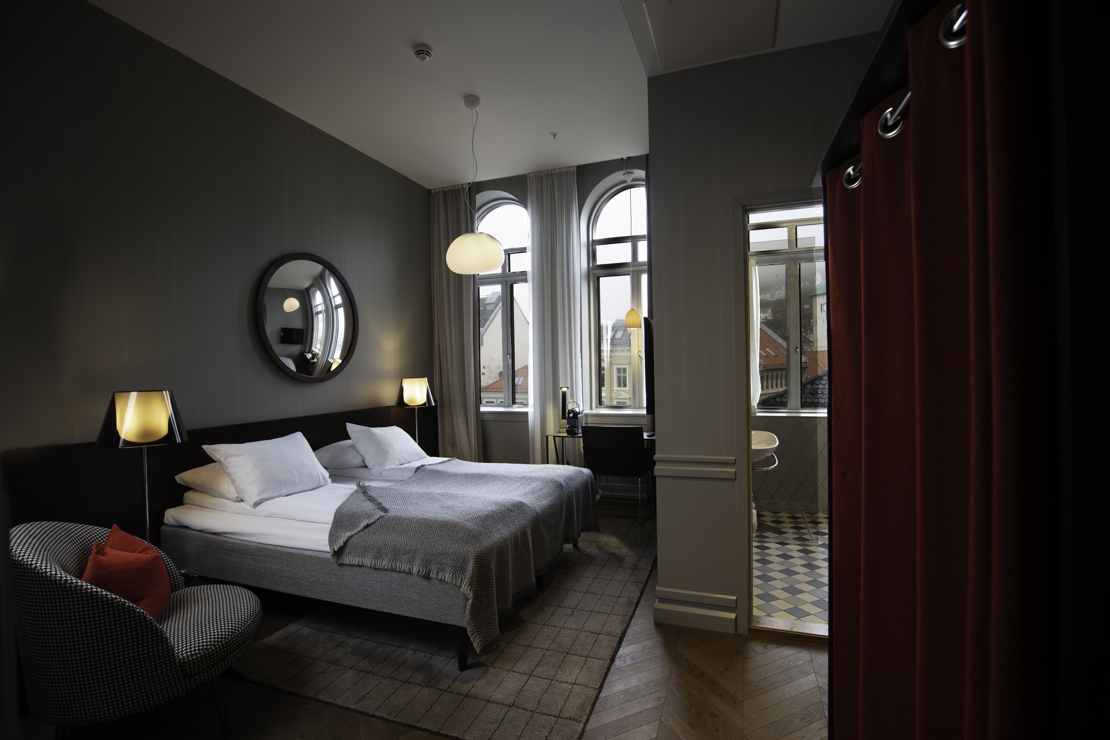 Quarto de hotel com duas camas, área de estar com uma poltrona, escrivaninha e banheiro visível por uma porta aberta.