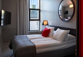 A hotel room with a bed, a TV, a window, and a mirror.