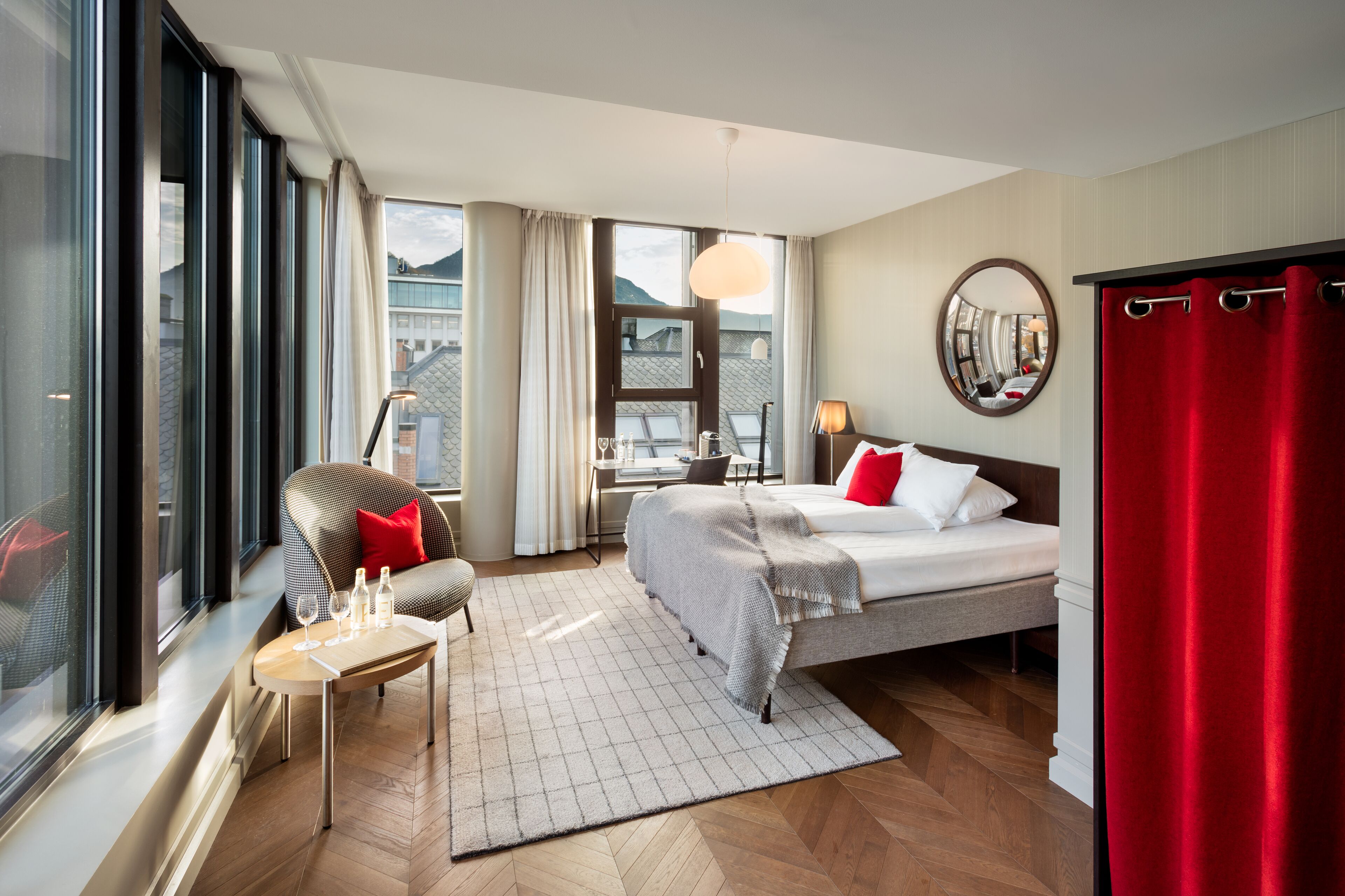 Ein Hotelzimmer mit einem Bett, einem Schreibtisch, einem Stuhl, einem Fenster und Blick auf Gebäude.