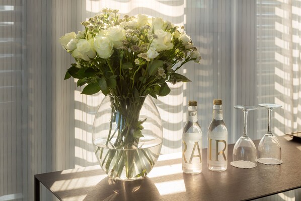 A clear glass vase with white flowers on a wooden table, next to a bottle and two wine glasses. - Bergen Børs Hotel (Bergen)