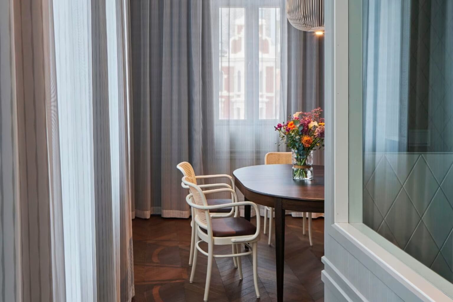 A dining area with a round table, two wicker chairs, and a vase of flowers.