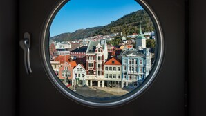 Vista a través de un ventanal redondo mostrando un pueblo con edificios coloridos y una colina al fondo.