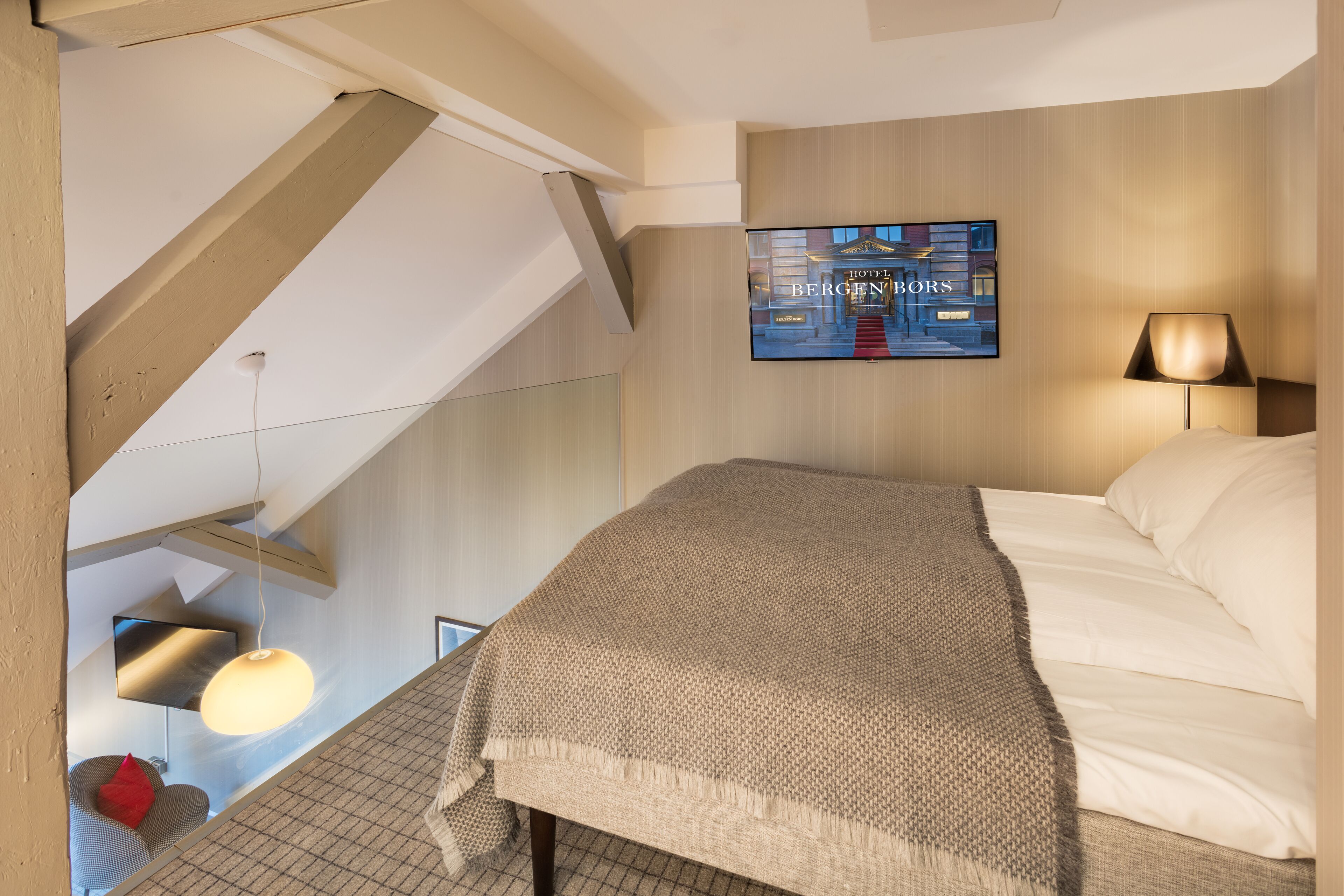 A hotel room with a bed, a TV mounted on the wall, and a lamp.