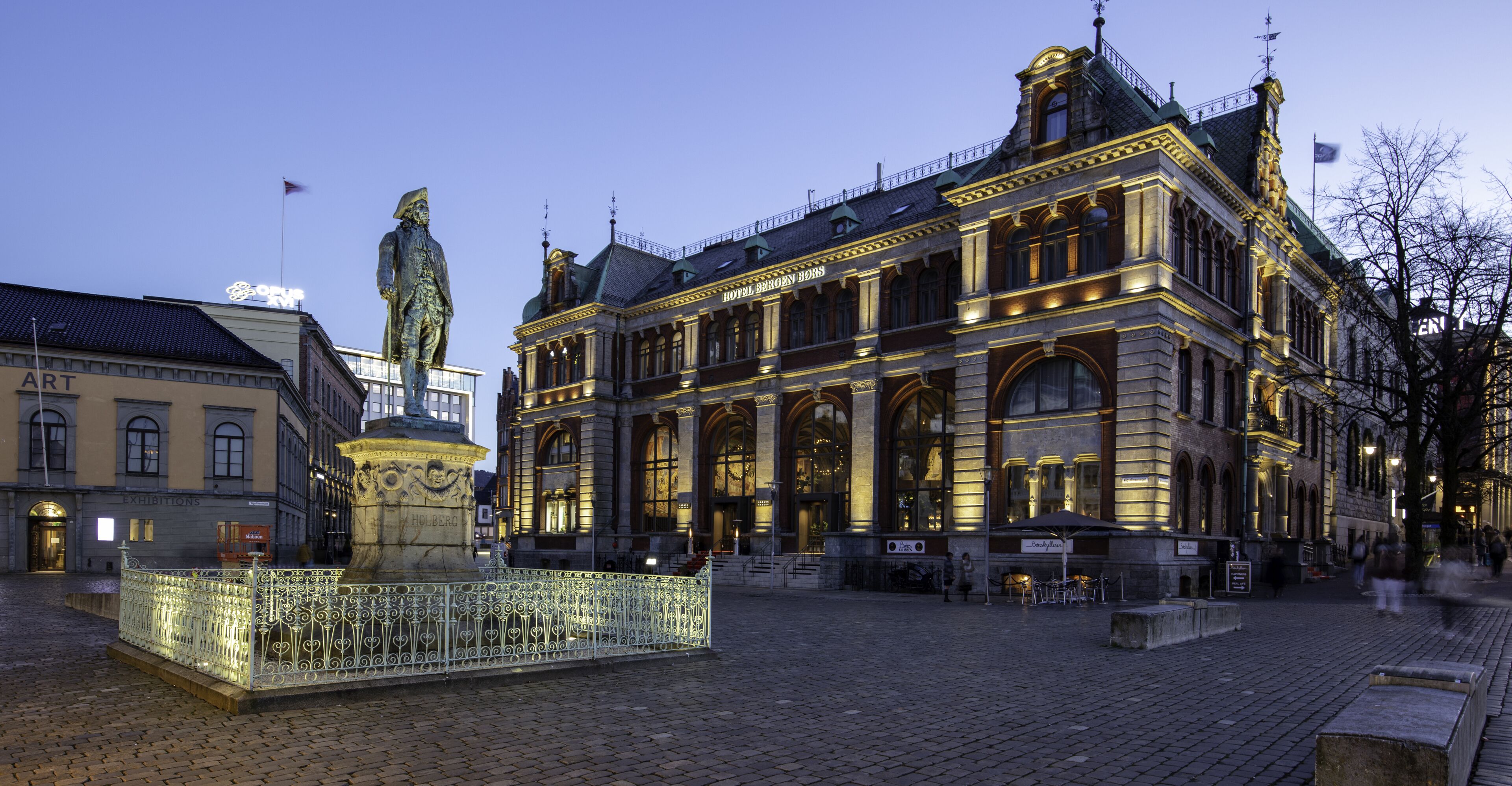A historic building with ornate architecture, a statue in the foreground, and a cobblestone plaza.