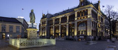 Un edificio histórico con arquitectura ornamentada, una estatua en primer plano y una plaza adoquinada.