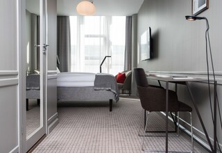A hotel room with a bed, a desk, a chair, a TV, and a large window with curtains.