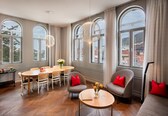 A spacious room with a large dining table, comfortable seating, and large windows offering views of the city.