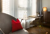 A modern hotel room with a sofa, a small table with a coffee maker, and a chair.