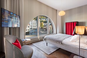A hotel room with a large curved window, a bed, a TV, and a chair with a red pillow. - Bergen Børs Hotel (Bergen)