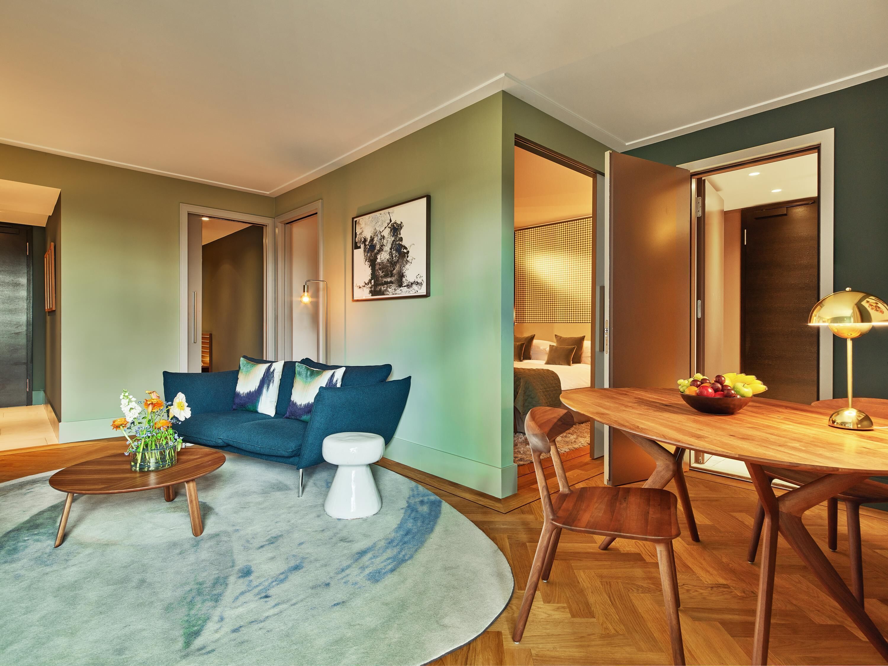 A modern living room with a blue sofa, a round coffee table, and a dining area with a wooden table and chairs.