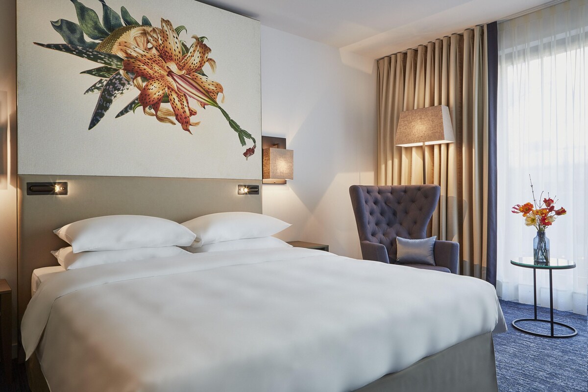 A hotel room with a large bed, a chair, a lamp, and a painting on the wall.