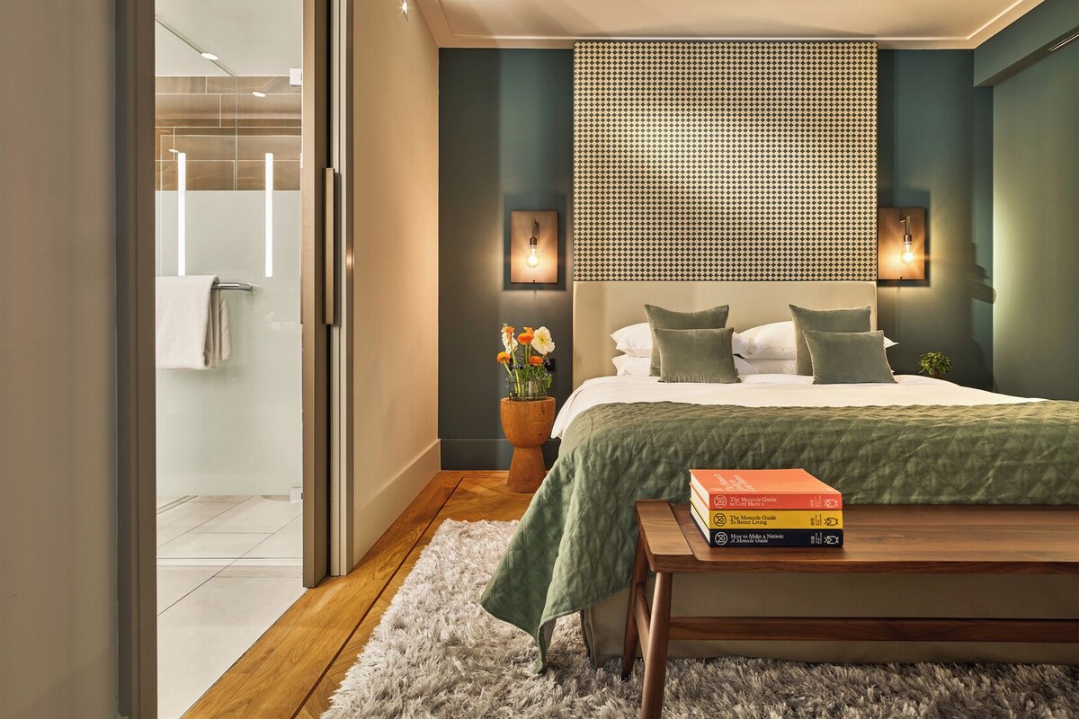 A modern bedroom with a bed, bedside lamps, a wooden nightstand, and a bookshelf.