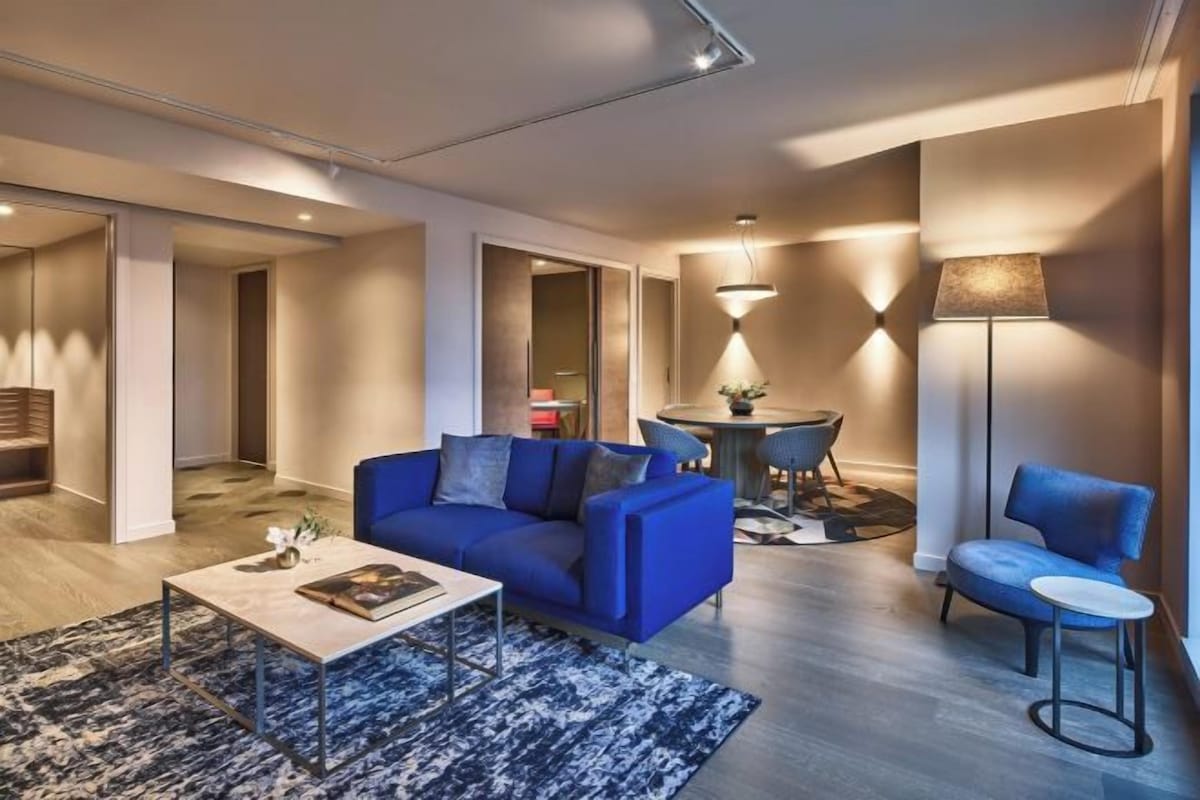 A modern living room with a blue sofa, a coffee table, and a dining area with a round table and chairs.