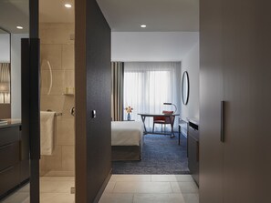 A hotel room with a bed, a desk, a chair, a mirror, and a window with curtains. - Hyatt Regency Amsterdam (Amsterdam)